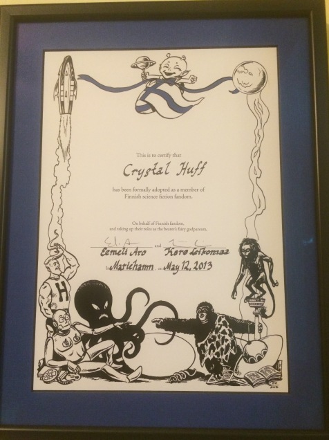My Finnish fannish adoption certificate, signed by Eemeli Aro and Karo Leikomaa. Finnish SFF characters around the border and an alien baby wrapped in a Finnish flag feature prominently in the art.